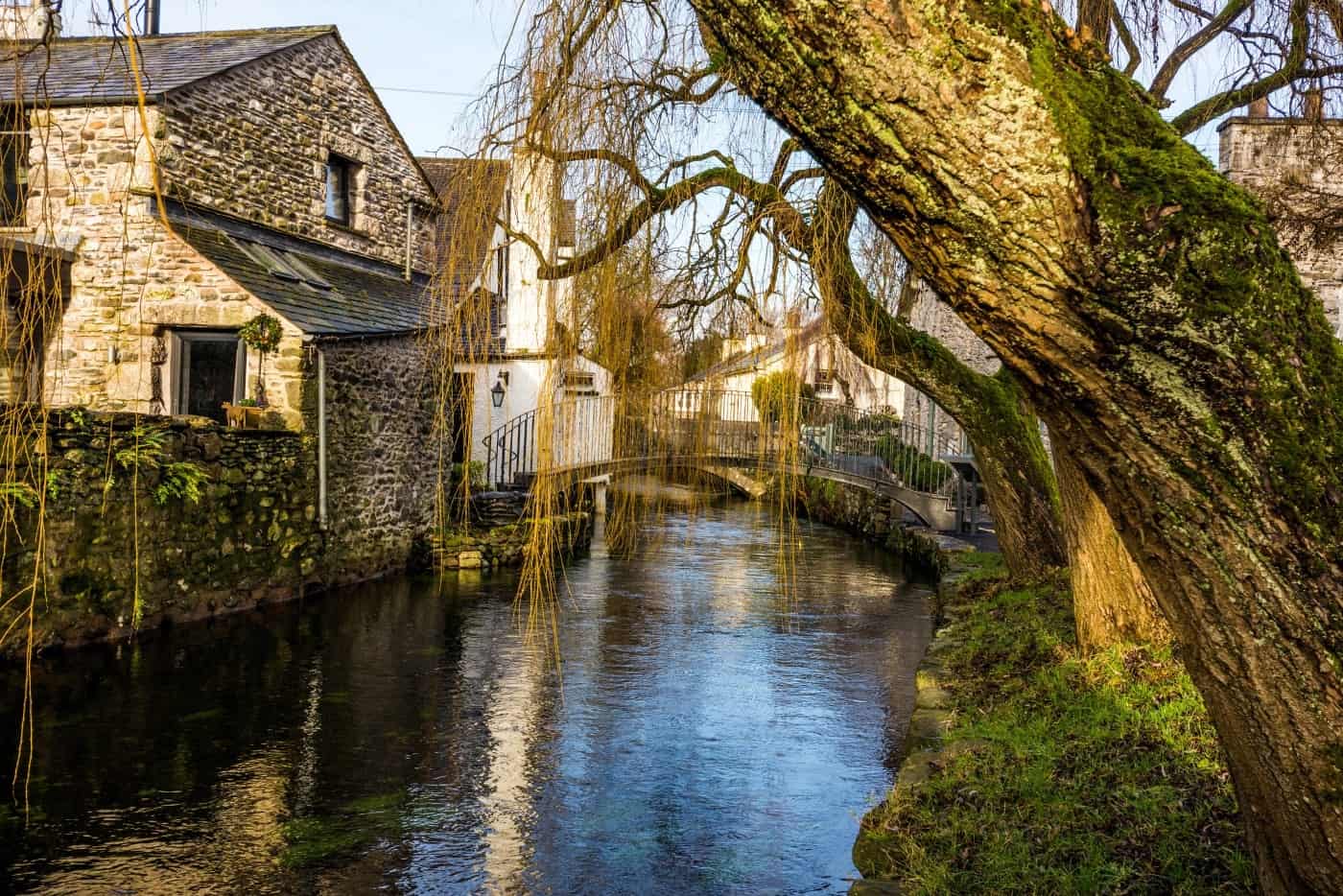 Stone cottages beside the River Eea in Cartmel village, with a willow tree overhanging the water